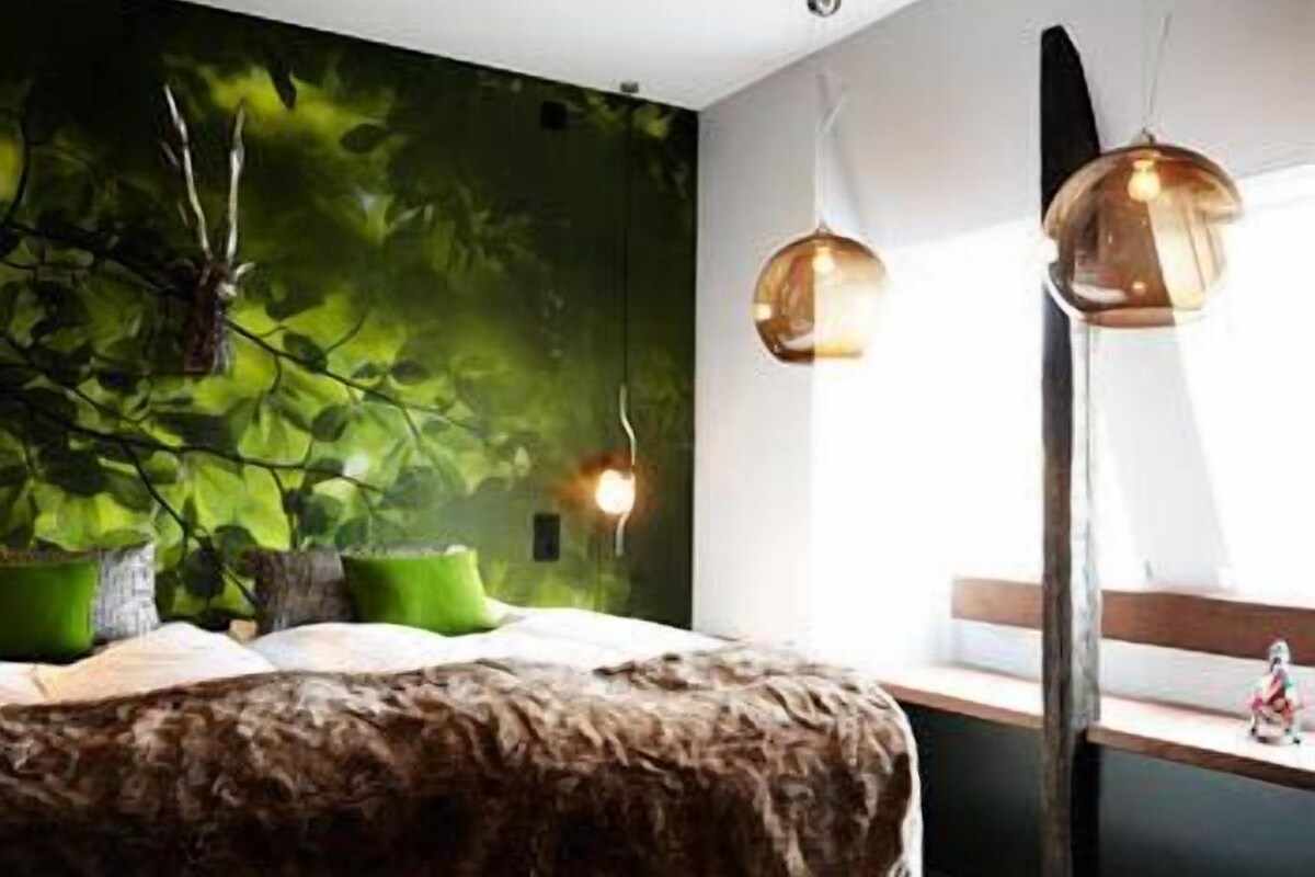 A modern bedroom with a large bed, a green plant wall, and two pendant lights.