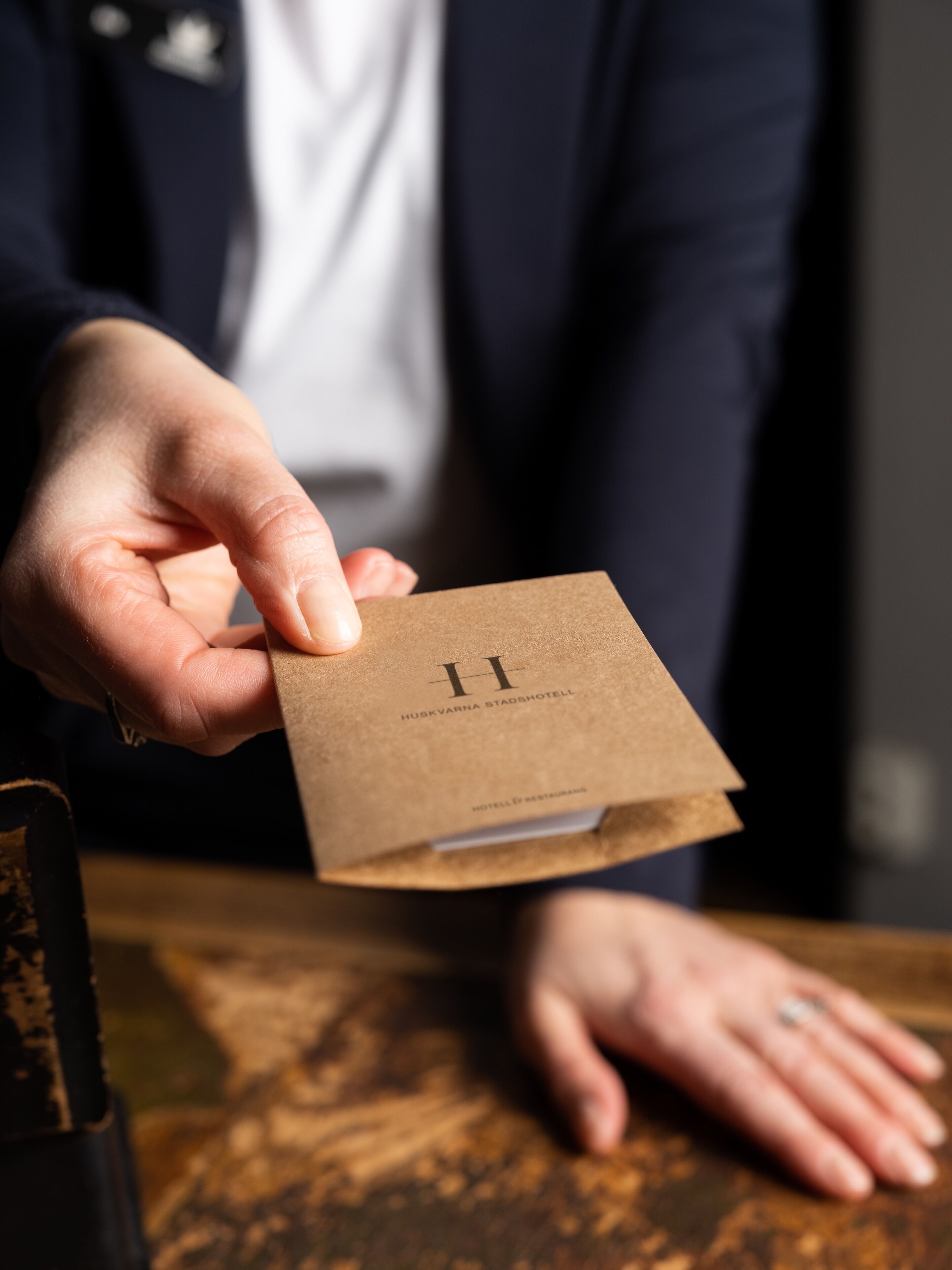 A hand holding a brown paper bag with the text "HUSKVARNA STADSHOTELL" and "HOTEL & RESTAURANTS" visible.
