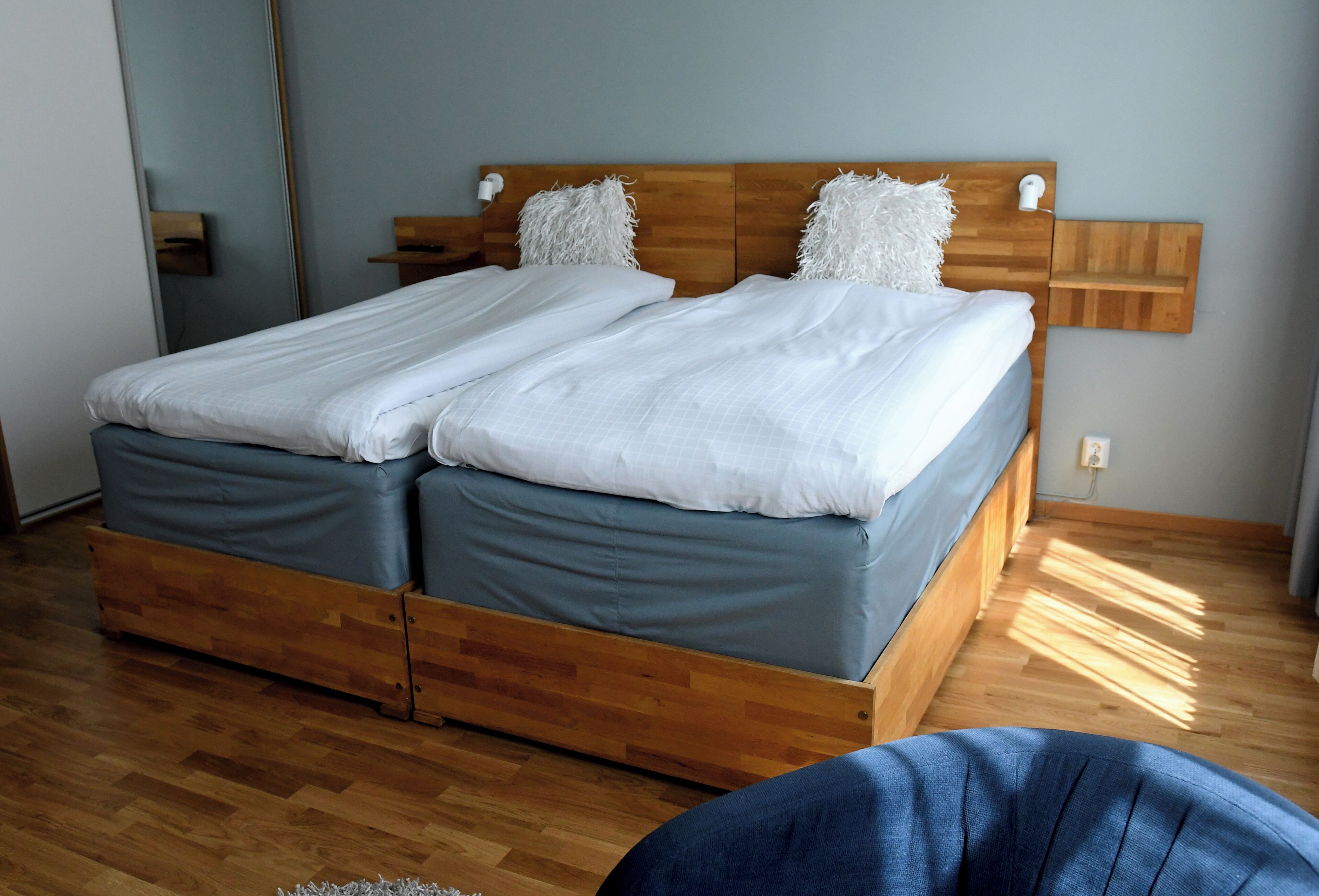 Cama doble con cabecera de madera y dos almohadas, suelo de madera y una mesita de noche.