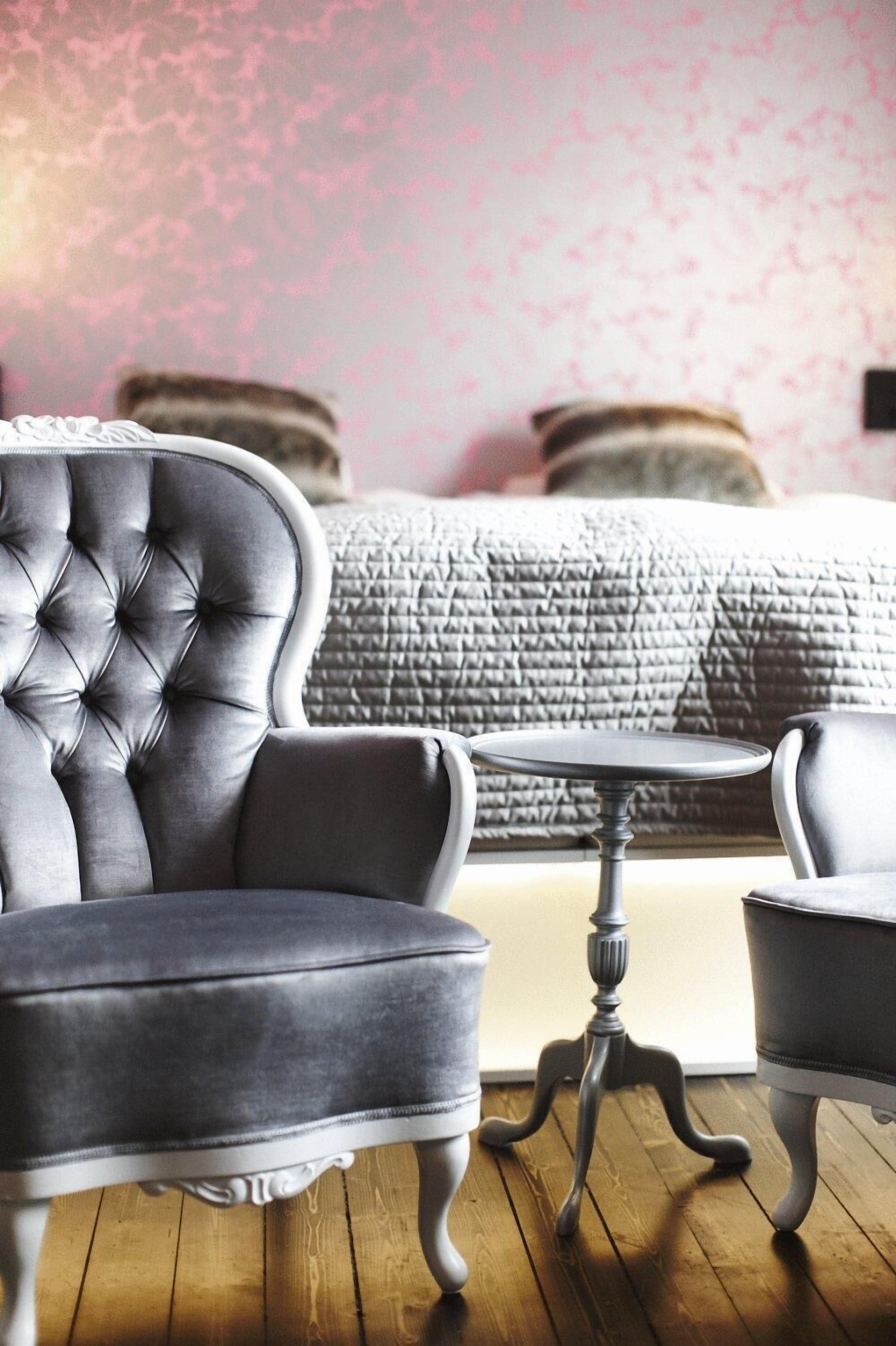 A room with a tufted armchair, a small round table, and a bed with a quilted headboard.