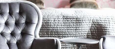 A room with a tufted armchair, a small round table, and a bed with a quilted headboard.