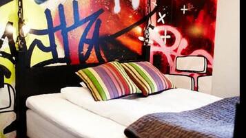 Un dormitorio con una cama, almohadas coloridas, un mural de estilo graffiti y luces colgantes.
