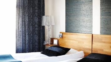 A hotel room with a wooden headboard, a bedside table with a lamp, and a large window with curtains.