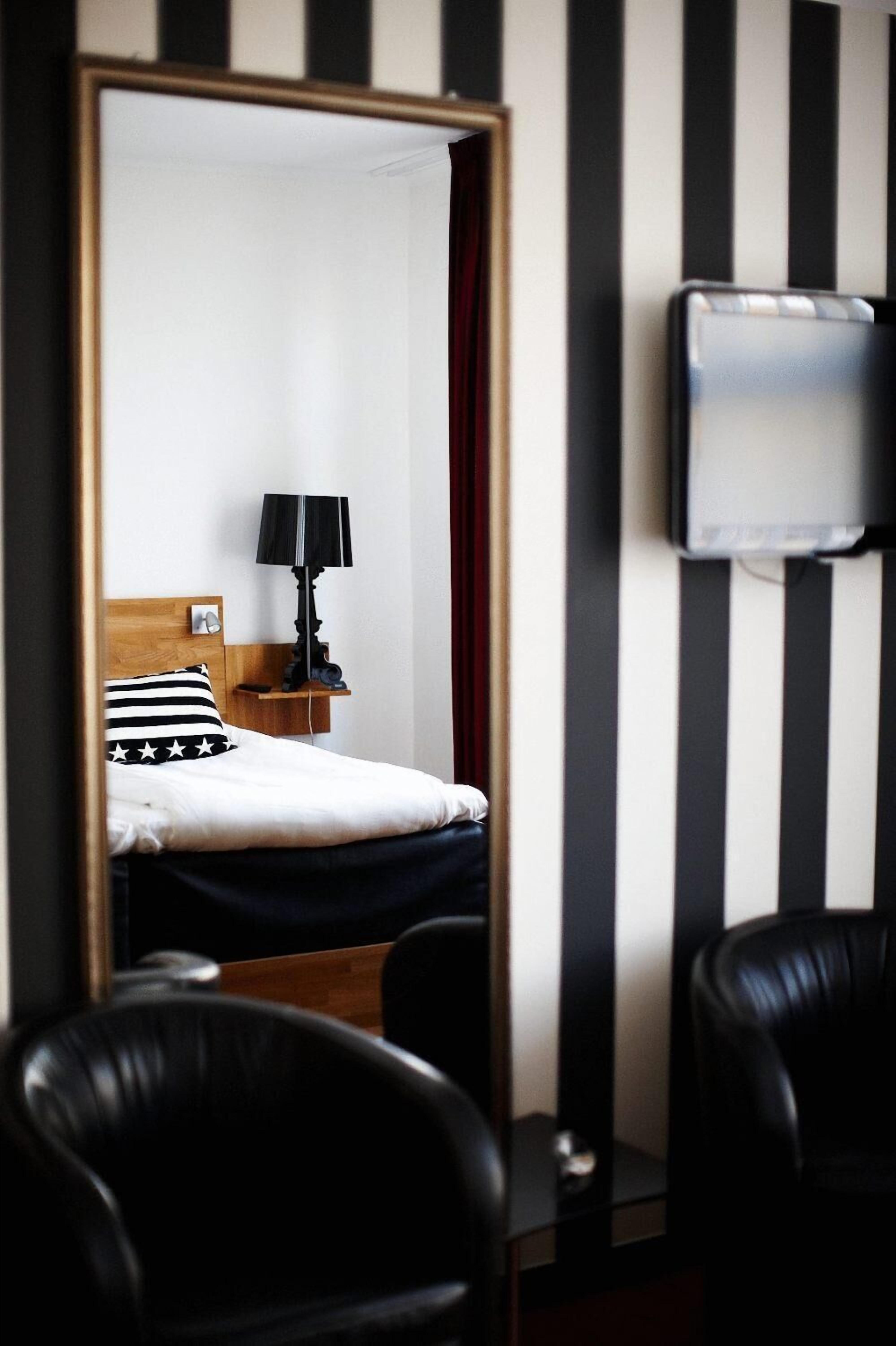 A hotel room with a bed, a nightstand, a lamp, a TV, and striped walls.