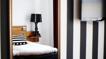 A hotel room with a bed, a nightstand, a lamp, a TV, and striped walls.