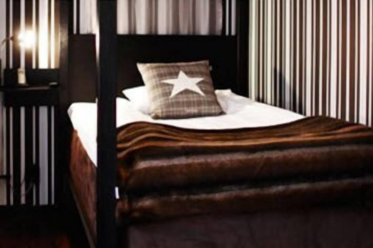 A bed with a star pillow, a striped wall, and a nightstand with a lamp.