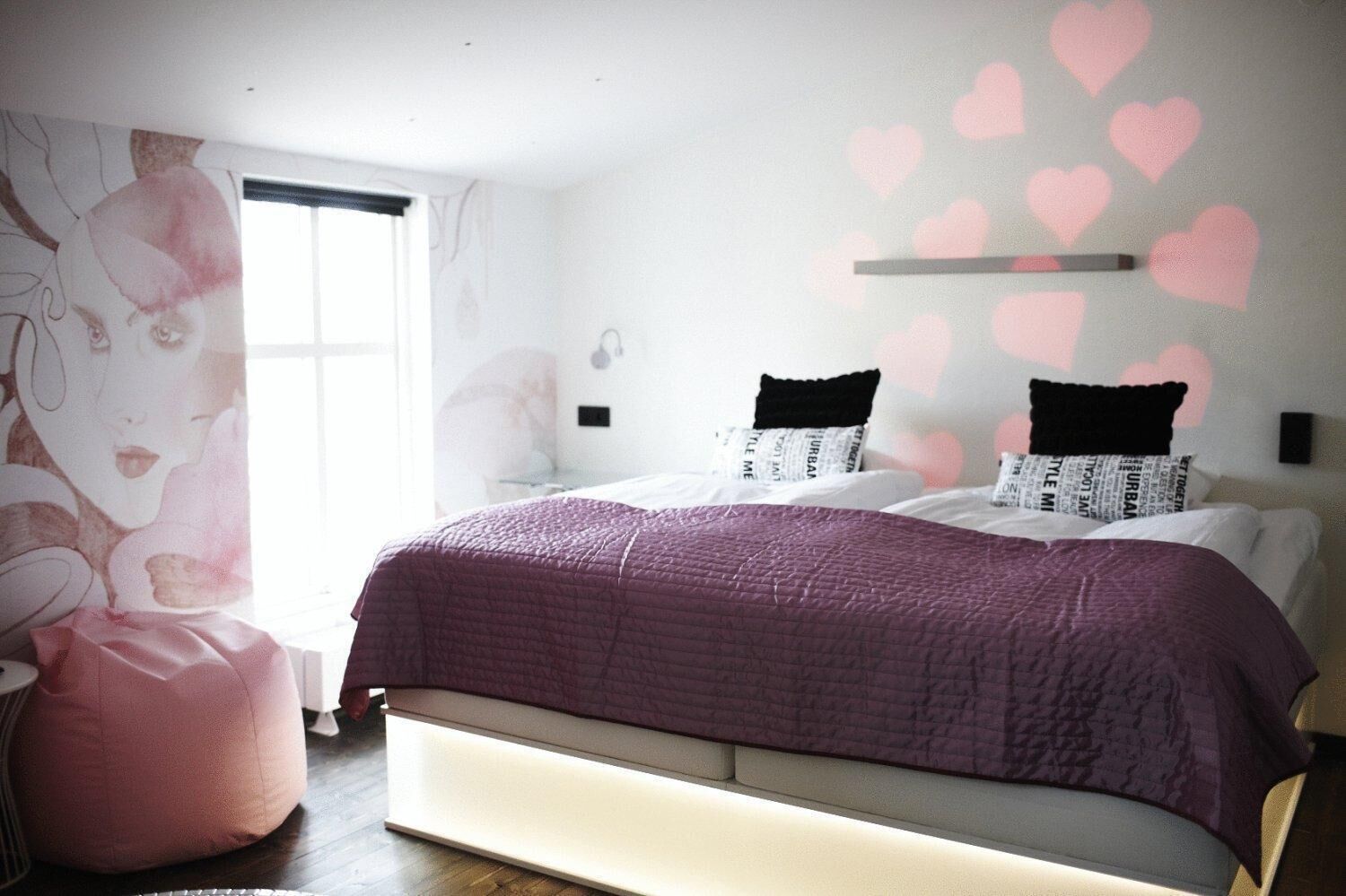 A bedroom with a large bed, a pink bean bag, and a wall with heart decorations.