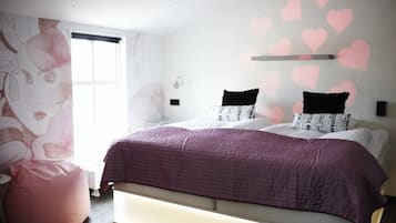 A bedroom with a large bed, a pink bean bag, and a wall with heart decorations.