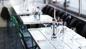 A restaurant with long tables set for dining, featuring candle centerpieces and clear glass bottles.