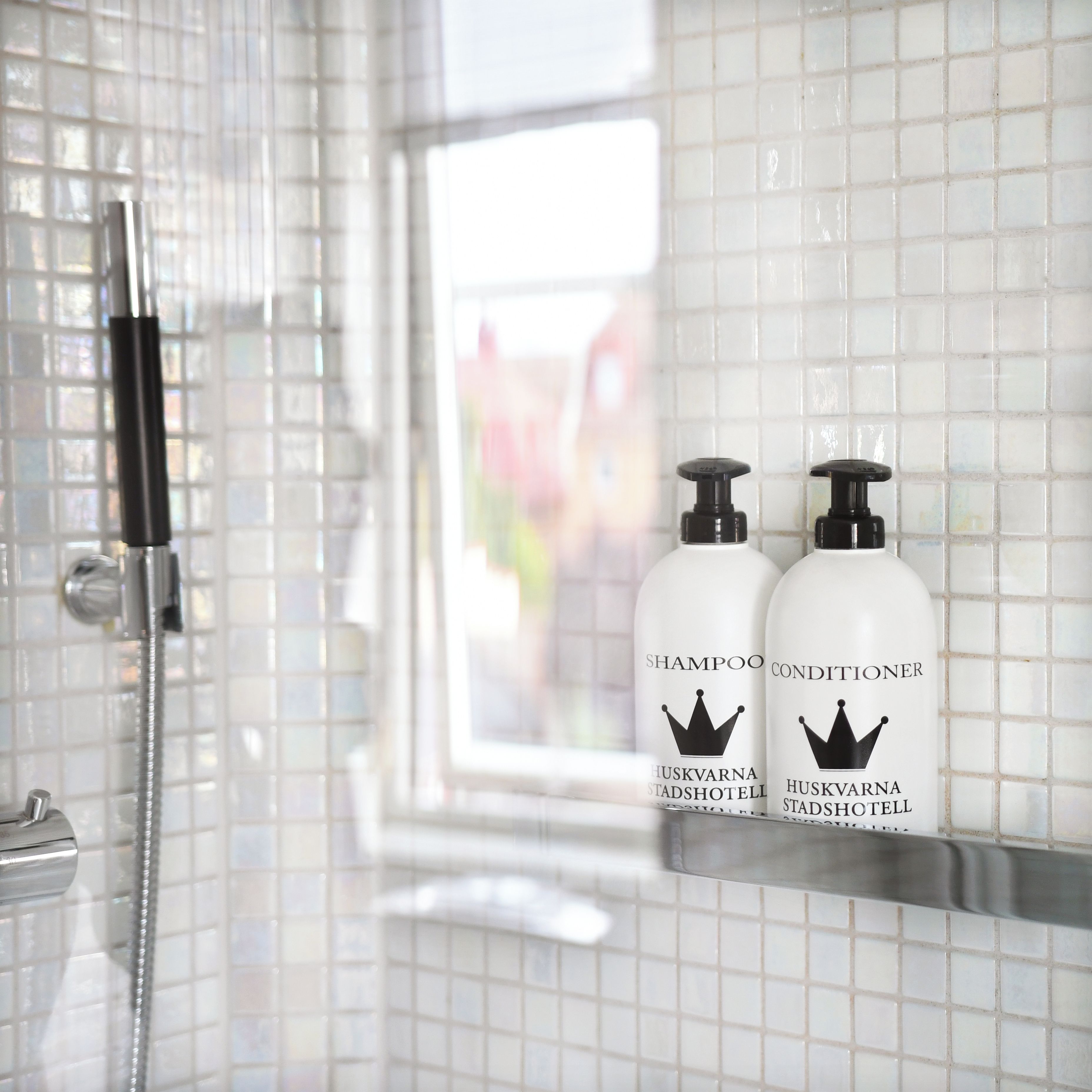 Un baño con paredes de azulejos blancos, una ducha y dos botellas de champú y acondicionador en un estante.