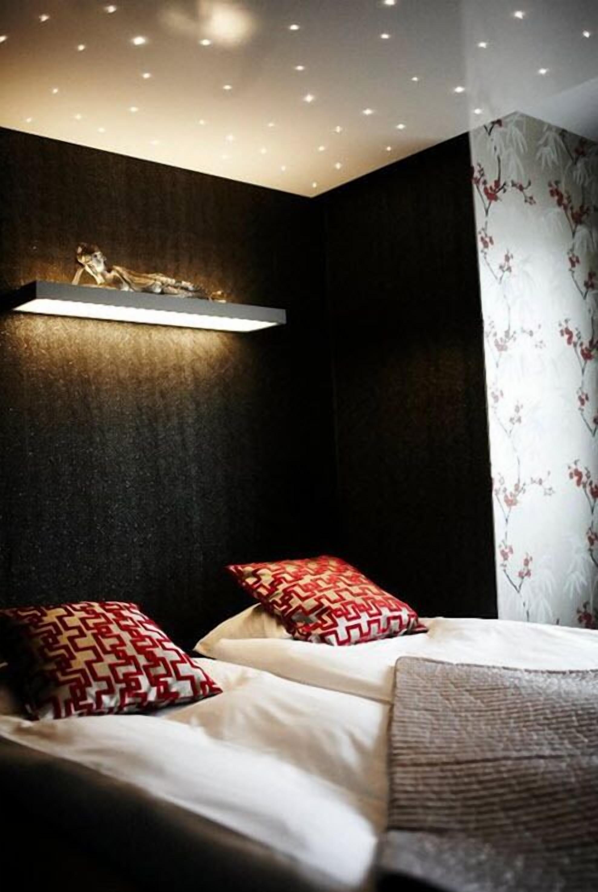 A modern bedroom with a bed, two patterned pillows, a wall-mounted light, and a floral curtain.