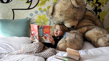 Una persona sentada en una cama con un oso de peluche grande y leyendo un libro.