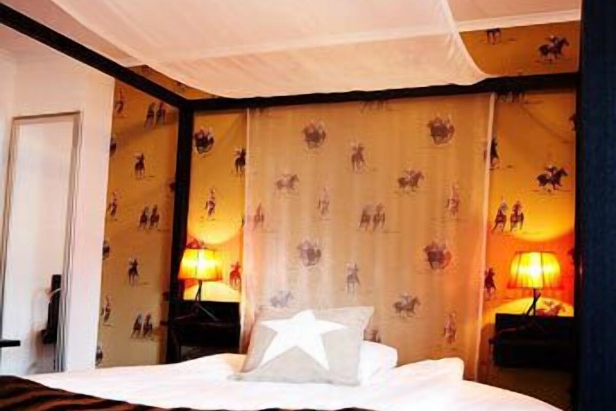 A hotel room with a bed, two bedside lamps, and a door.