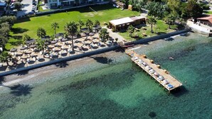 An aerial view of a resort with a pier extending into clear waters, a pool area with sun loungers, and a building with a red roof. - Hotel Akbulut (Kusadasi)
