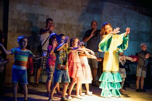 Un gruppo di bambini e adulti in una stanza scarsamente illuminata, con pareti in pietra.