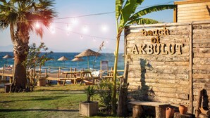A wooden sign with the text "beach of AKBULUT" and a beach setting with palm trees, umbrellas, and lounge chairs. - Hotel Akbulut (Kusadasi)