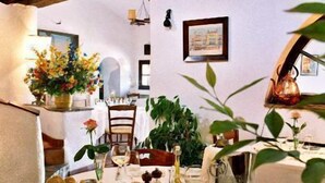 A dining table set with plates, glasses, and a pitcher, surrounded by chairs and a vase of flowers. - Moulin de la Camandoule (Fayence)