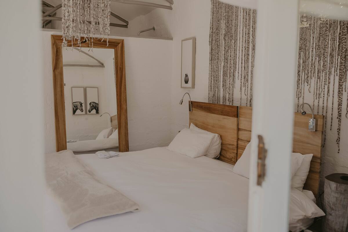 Un dormitorio con cabecera de madera, ropa de cama blanca, un espejo y una lámpara colgante.
