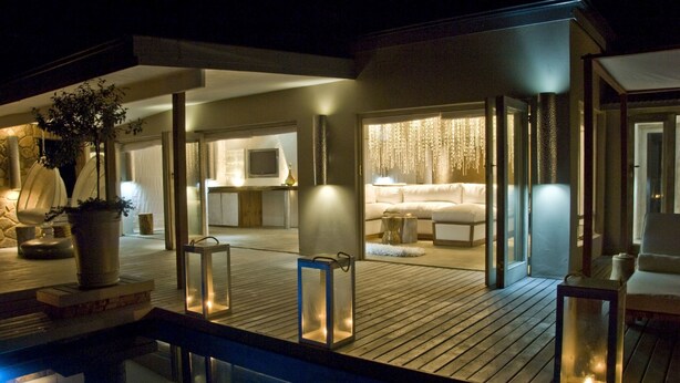 A modern, well-lit outdoor area with a pool, wooden deck, and seating areas.