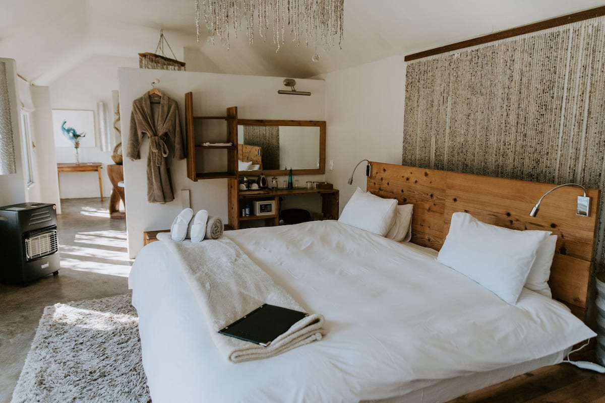 Un dormitorio con una cama grande, cabecera de madera, mesitas de noche, un espejo y perchero.