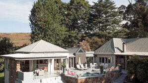 A house with a covered patio, outdoor seating, a swimming pool, and a stone wall.