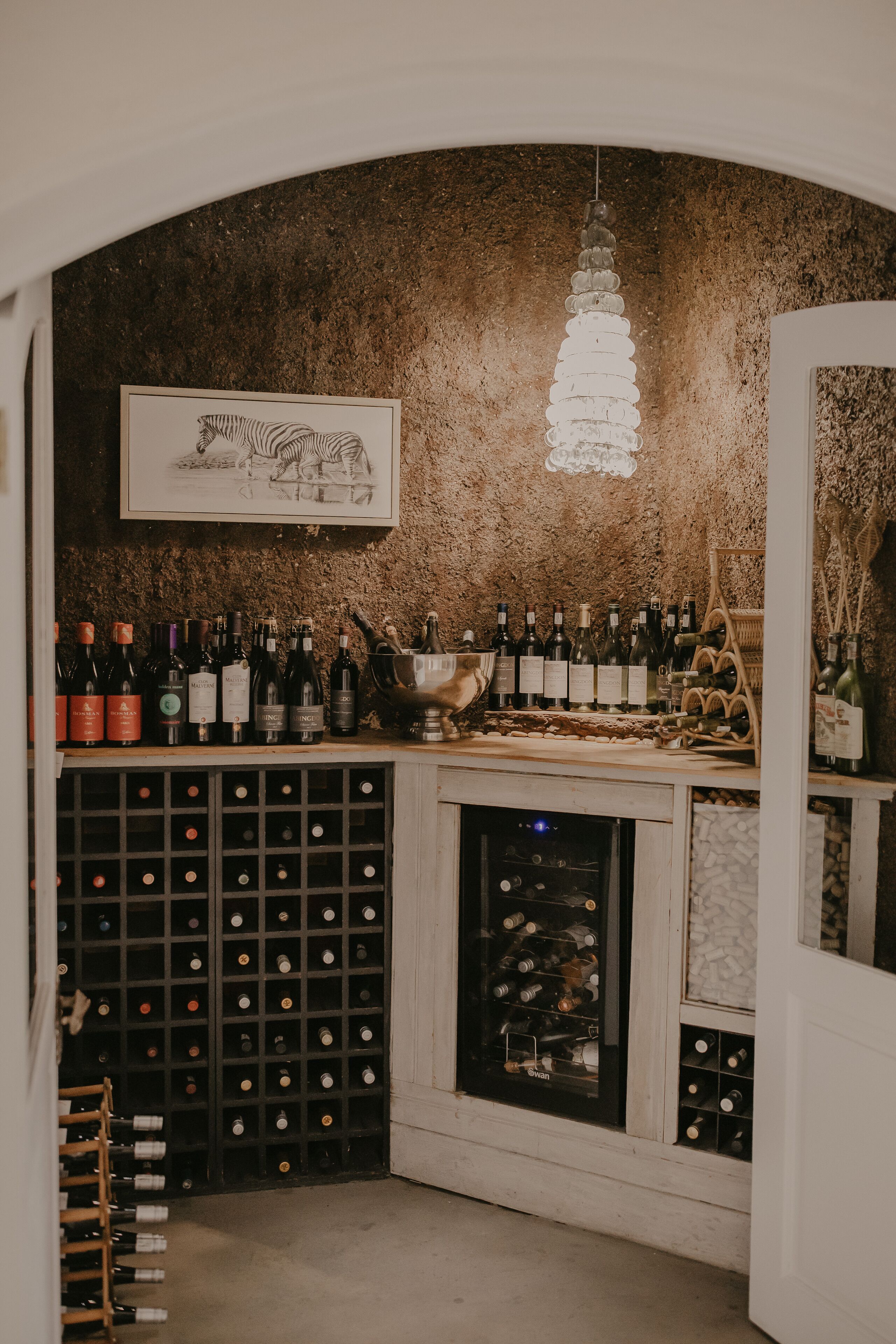 A wine cellar with a wooden wine rack, a wine cooler, and a framed artwork on the wall.