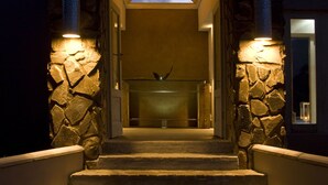A stone entrance with steps leading to a covered area, illuminated by wall-mounted lights.
