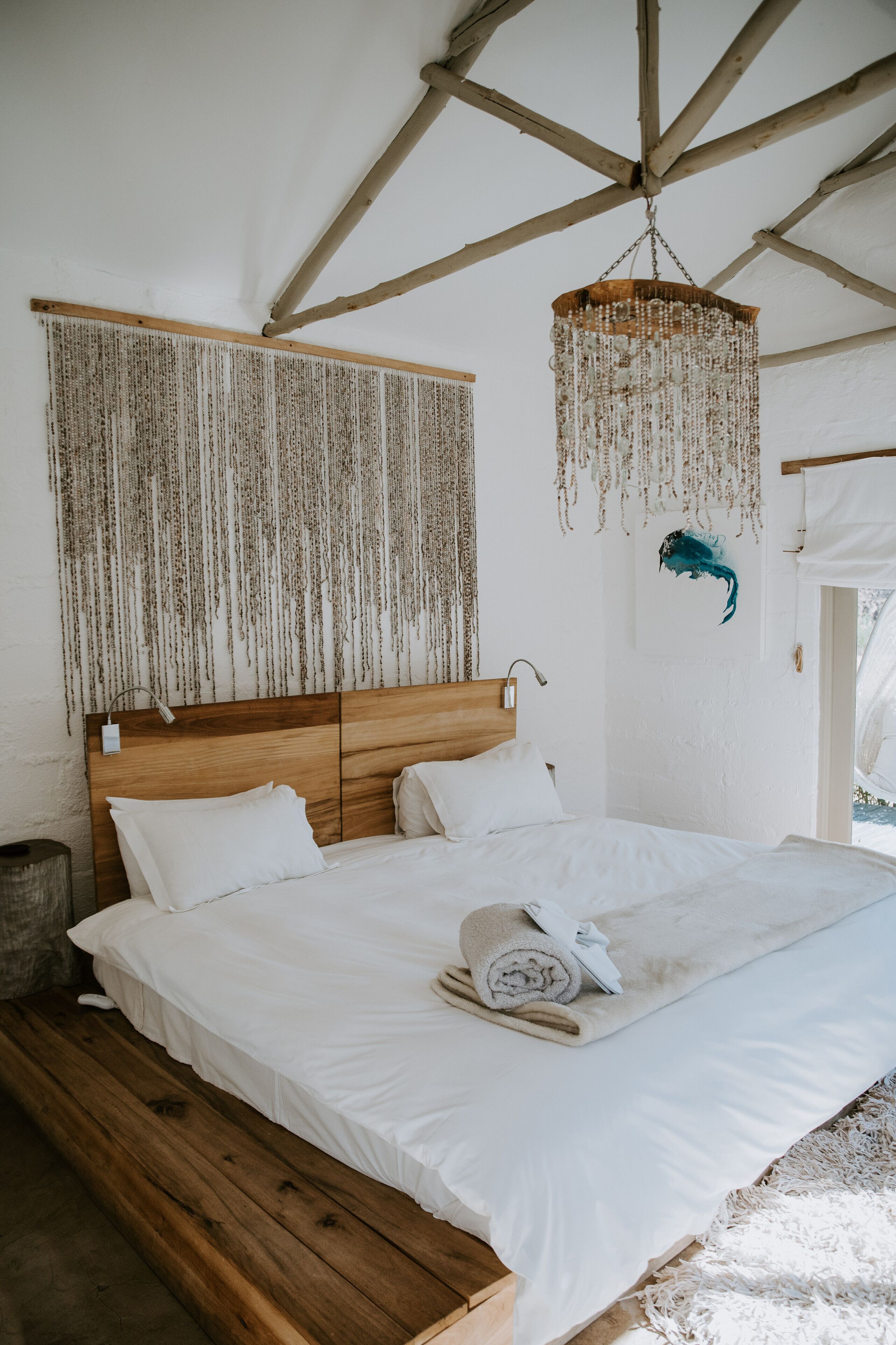 Ein Schlafzimmer mit einem Holzkopfende, weißer Bettwäsche, einem hängenden Chandelier und einer Wandteppich.