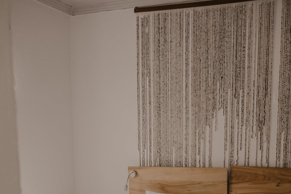 Un dormitorio con cabecera de madera, ropa de cama blanca y un tapiz de pared con textura.