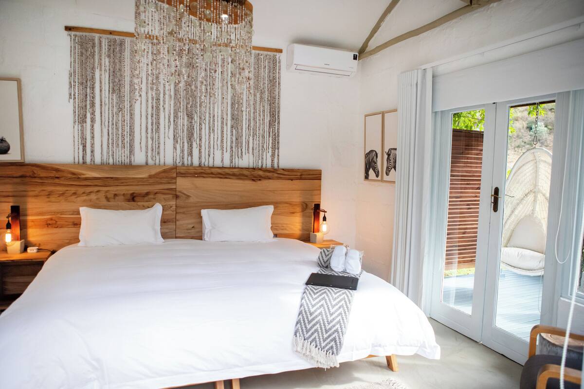 Un dormitorio amplio con una cama grande, cabecera de madera y vista a una terraza de madera a través de un ventanal corredero.