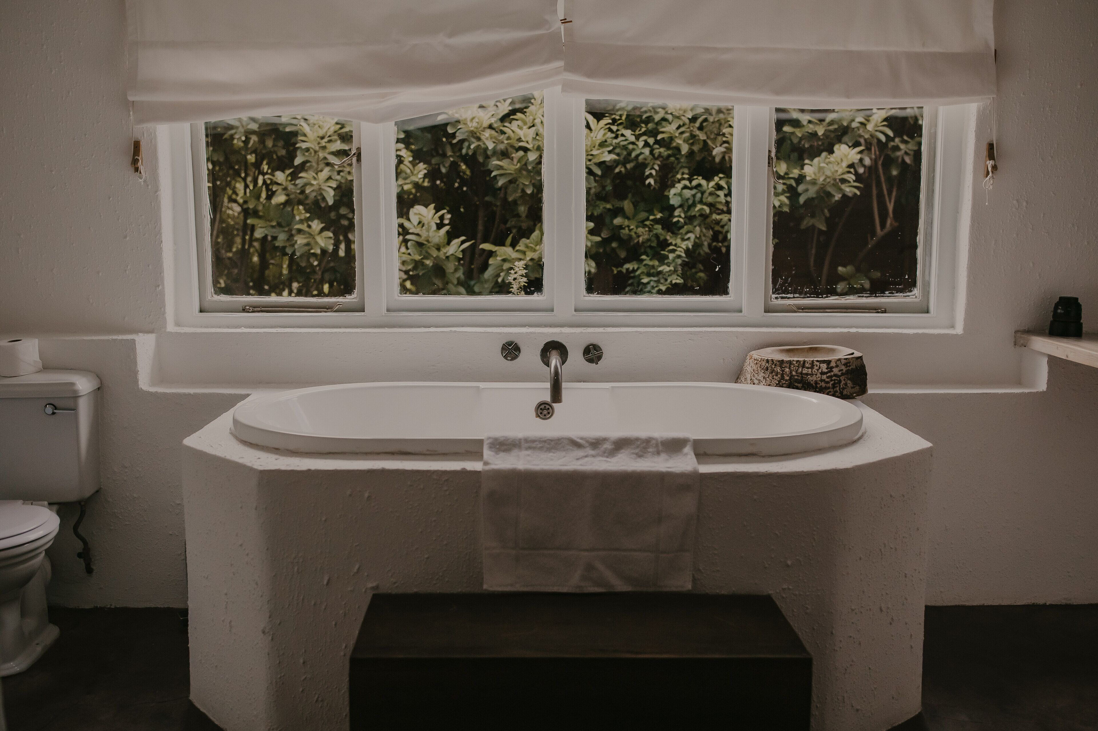 A bathroom with a freestanding bathtub, a toilet, and a window with a view of greenery.