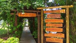 A wooden archway with signs hanging on it, surrounded by greenery. - Praia Sol Hotel (Santa Terezinha do Itaipu)
