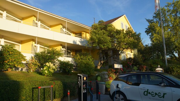 Une voiture blanche, ornée du logo « deer », est garée devant un immeuble jaune doté de balcons.