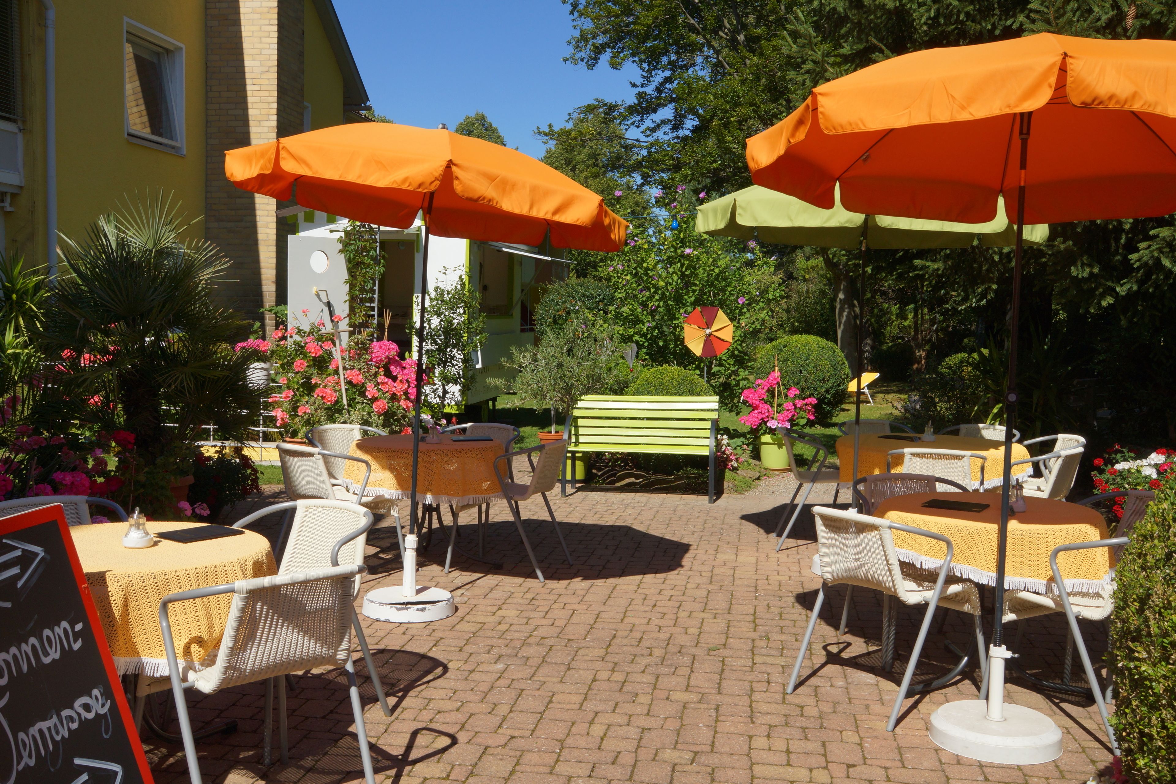 An outdoor patio area with tables and chairs, orange umbrellas, and a green bench.