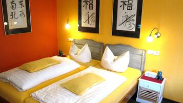 A hotel room with two beds, each with white linens and yellow pillows. There are framed calligraphy pieces on the walls and a small nightstand with a lamp.