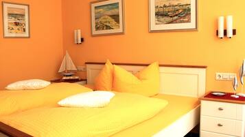 A hotel room with a large bed, two paintings on the wall, a nightstand with a lamp, and a dresser with drawers.