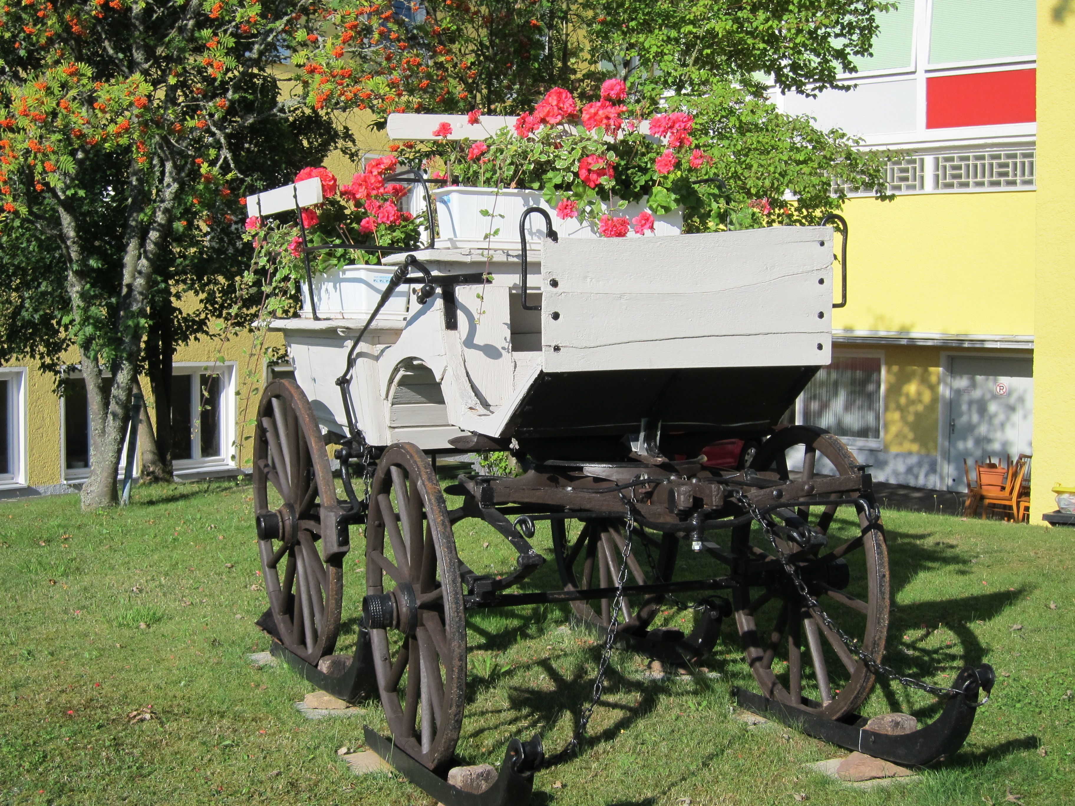 A vintage carriage parked on grass with a building in the background.