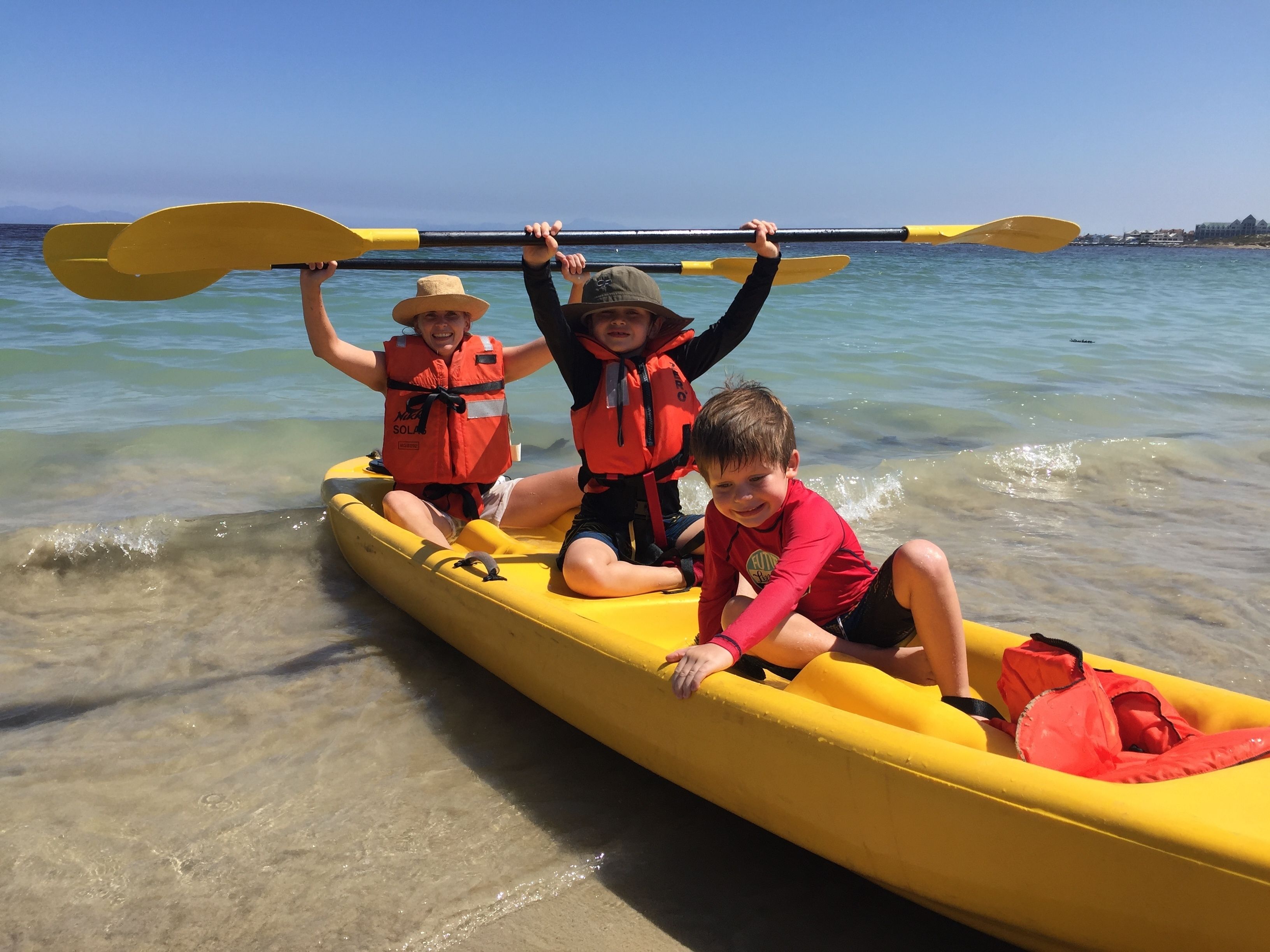 Three people in a yellow canoe on a calm body of water.