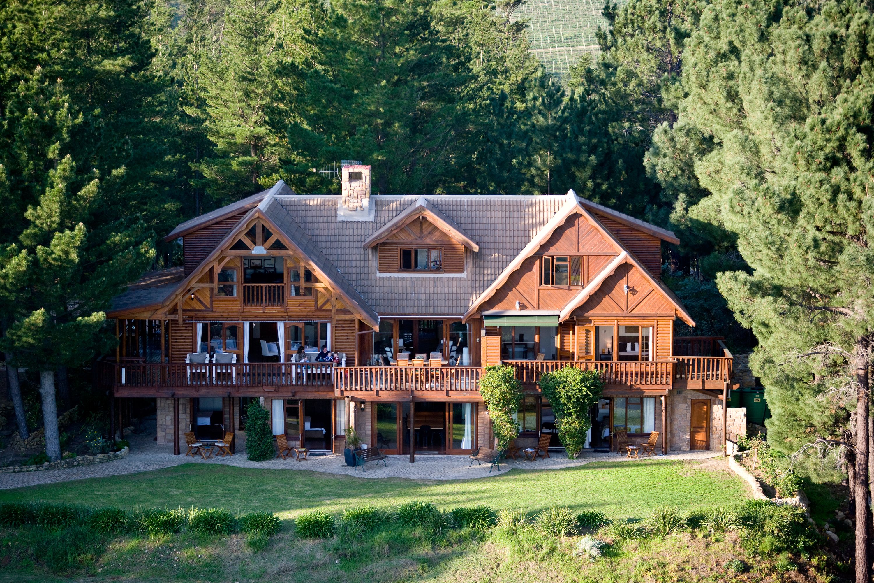 A large wooden cabin with a spacious deck, multiple windows, and a well-maintained lawn.