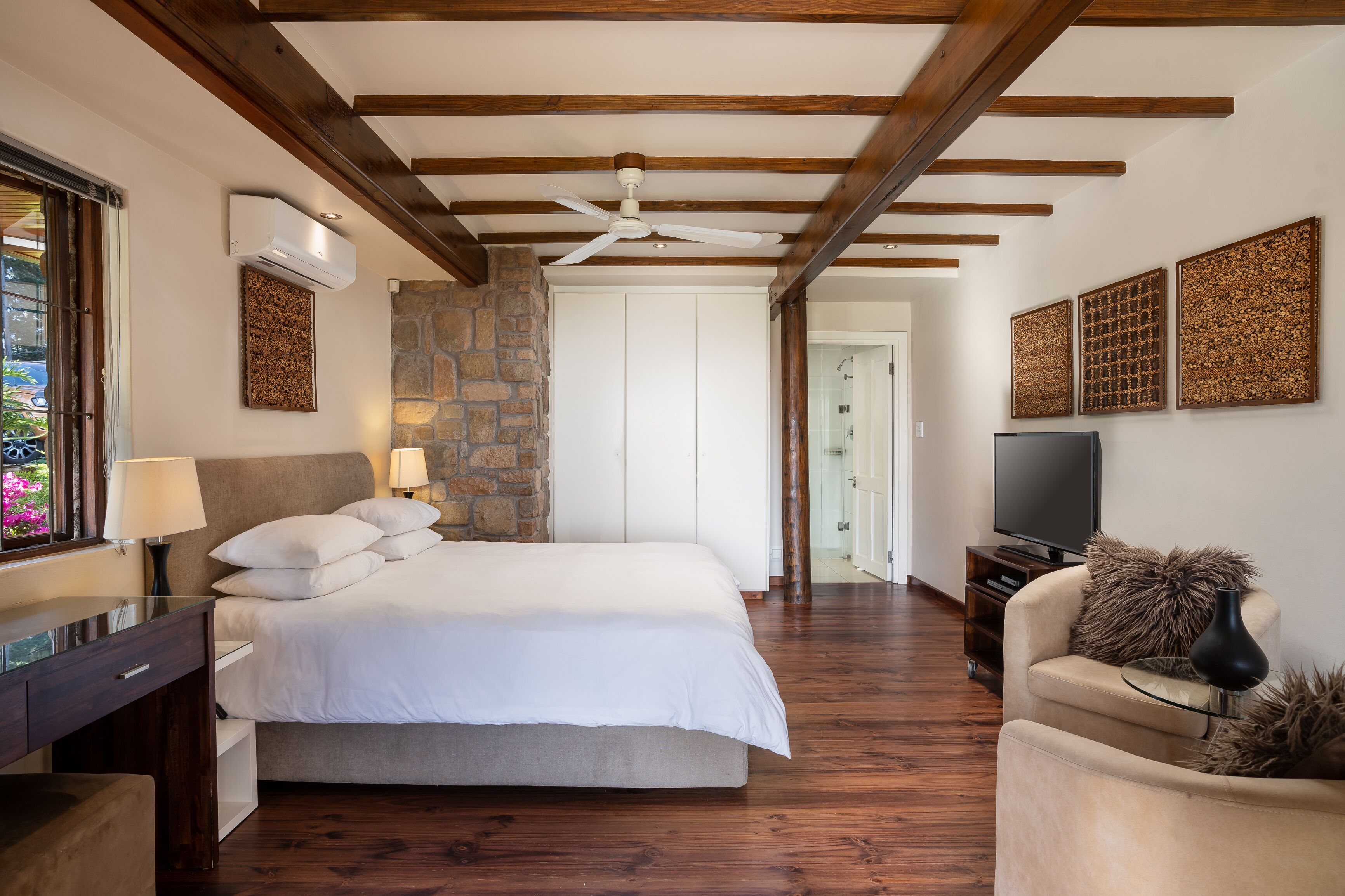 A bedroom with a bed, bedside tables, a TV, and a stone wall.