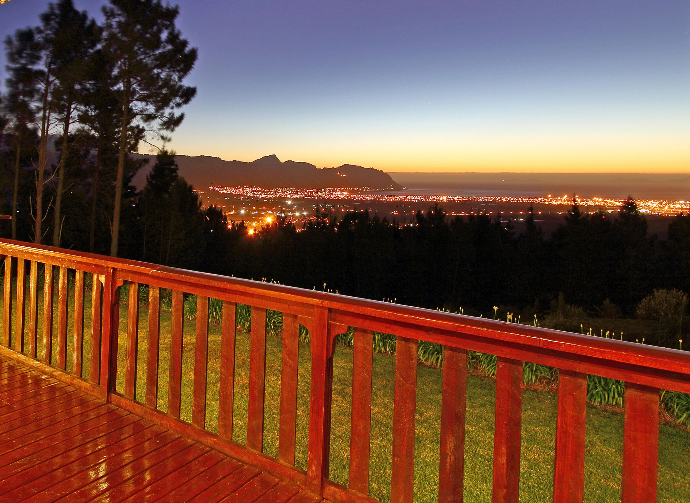 A wooden deck with a railing overlooking a cityscape at dusk.