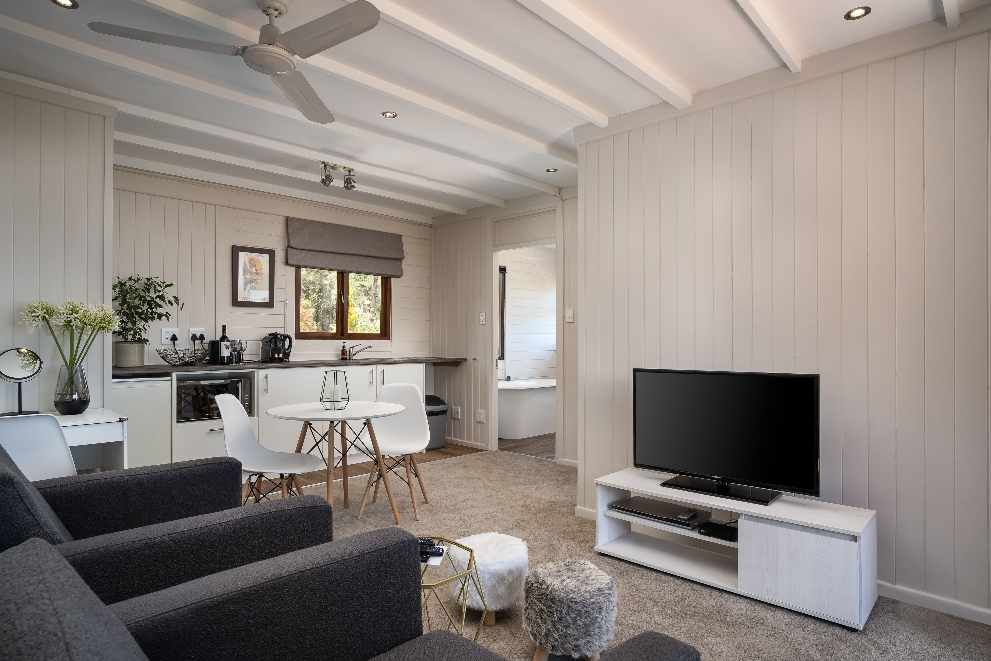 A modern living room with a flat-screen TV, grey sofas, and a dining area with a white table and chairs.