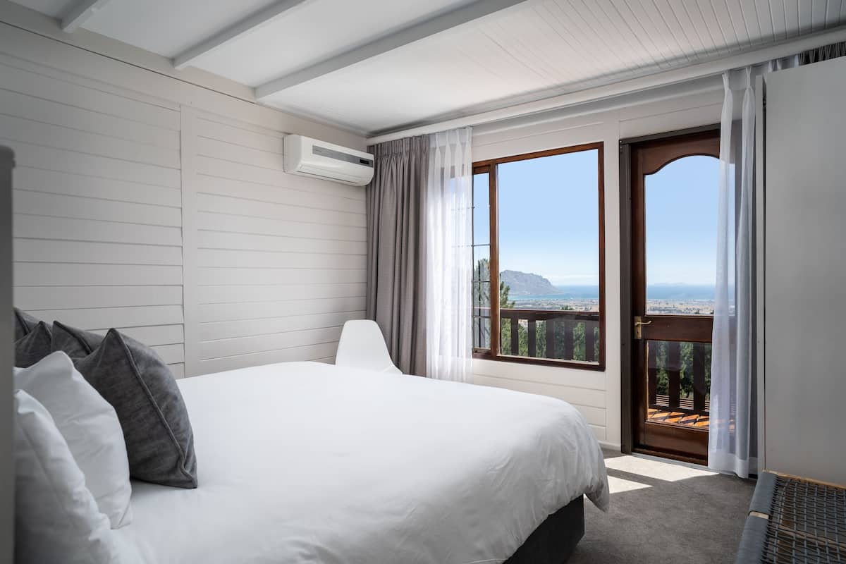 A hotel room with a large bed, a view of the mountains, and a balcony with a wooden railing.