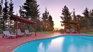 A swimming pool with lounge chairs and a pergola, surrounded by trees. - Lalapanzi Lodge (Cape Town)