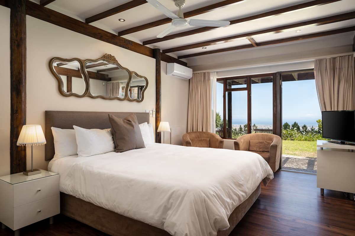 A hotel room with a large bed, a TV, a ceiling fan, and a view of the outdoors.