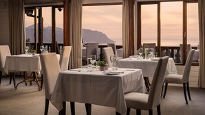 A dining area with tables set for four, large windows with curtains, and a view of mountains. - Lalapanzi Lodge (Cape Town)