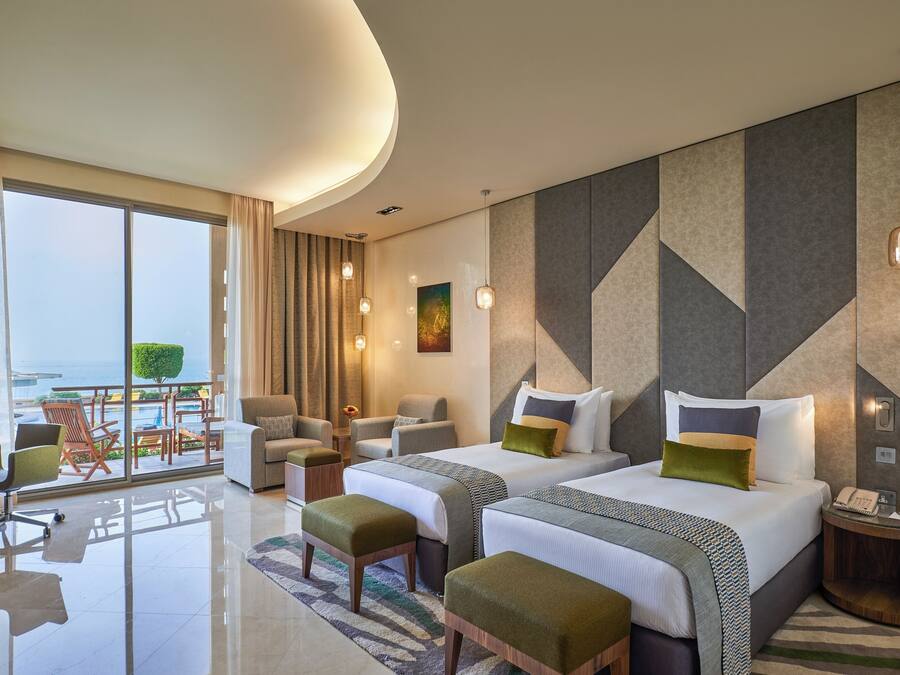 A hotel room with two beds, a balcony with chairs, and a view of the sea.