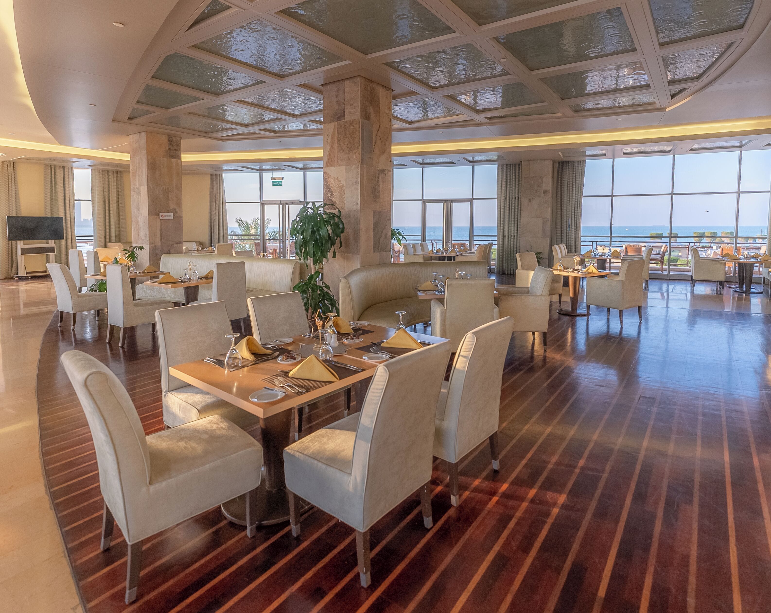 A spacious dining area with high ceilings, large windows, and a view of the ocean.