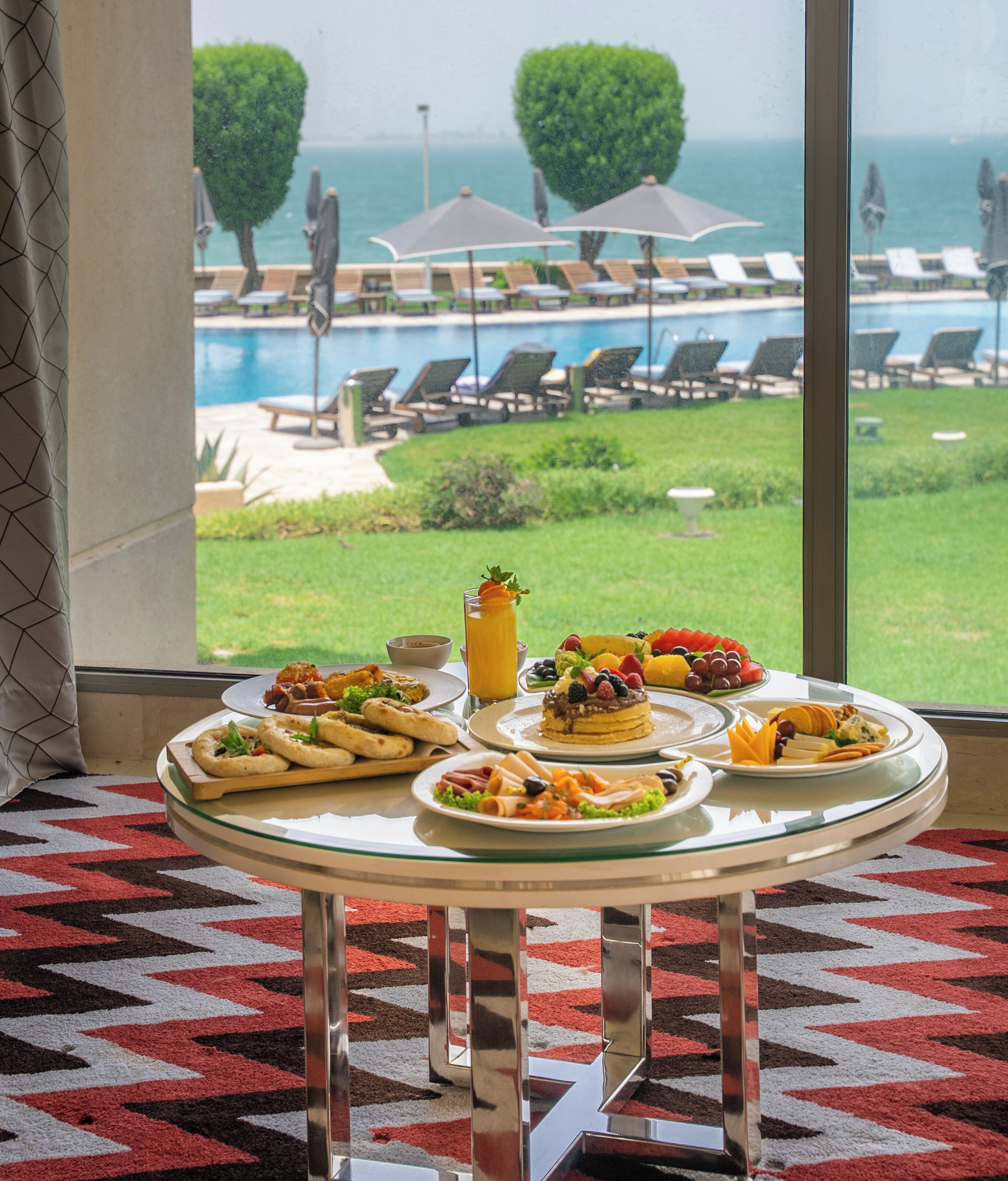 A dining table with breakfast items and a view of a pool and lounge chairs.