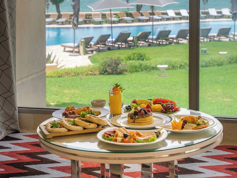 A dining table with breakfast items and a view of a pool and lounge chairs.